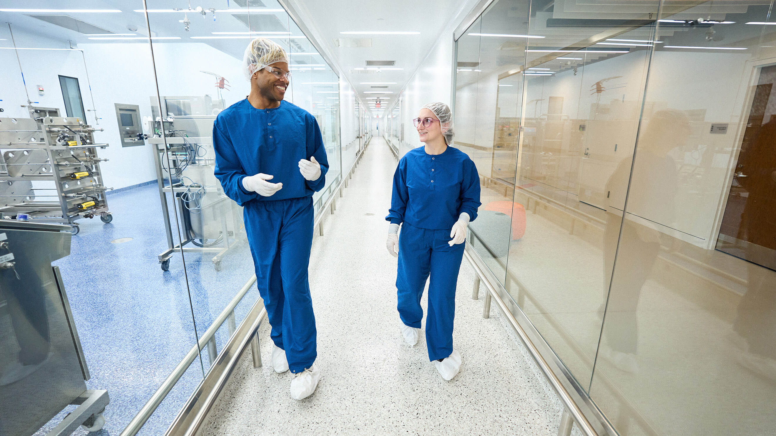 Man and woman dressed in scrubs walk down lab hallways